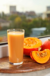 Photo of Tasty pumpkin juice in glass, whole and cut pumpkins on windowsill indoors