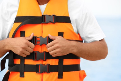 Photo of Male lifeguard putting on life vest near sea, closeup