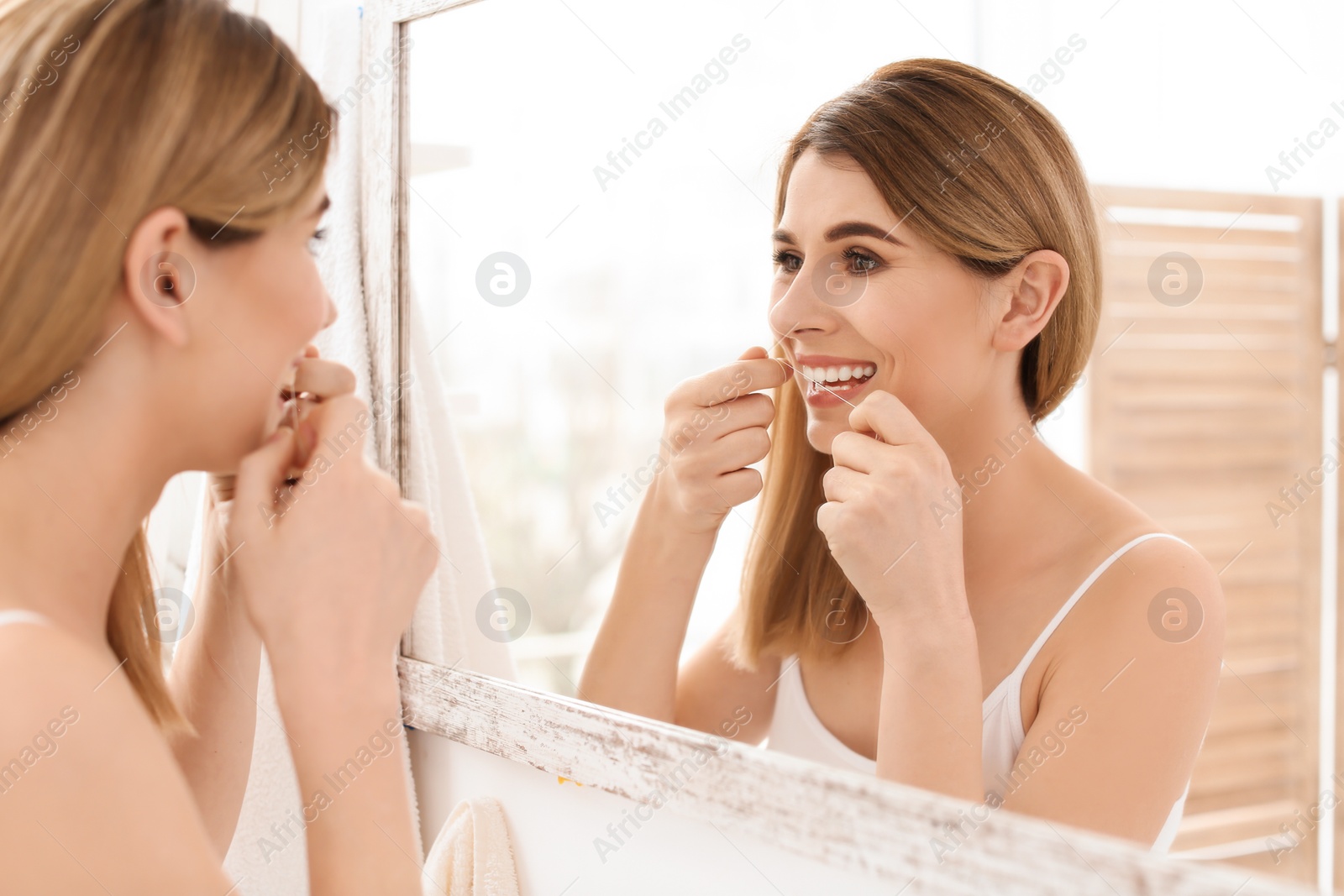 Photo of Young woman flossing her teeth in bathroom