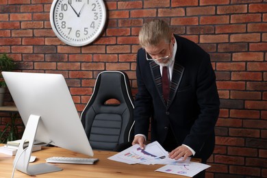 Senior boss working with paper sheets at wooden table in modern office