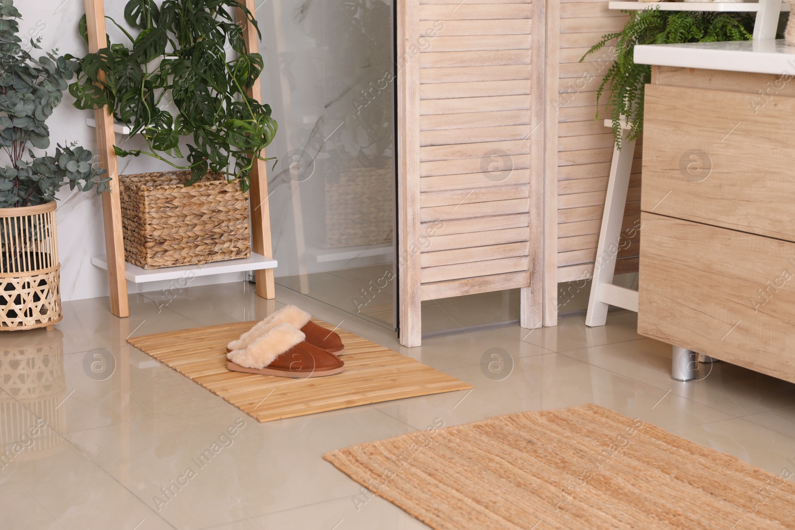 Photo of Wooden mat and slippers on tiled floor in bathroom. Stylish accessory