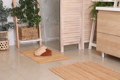 Wooden mat and slippers on tiled floor in bathroom. Stylish accessory