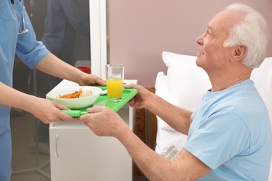 Photo of Nurse giving tray with food to senior patient in hospital ward. Medical assisting