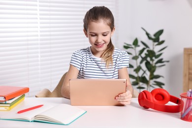 Photo of E-learning. Cute girl using tablet for studying online at table indoors