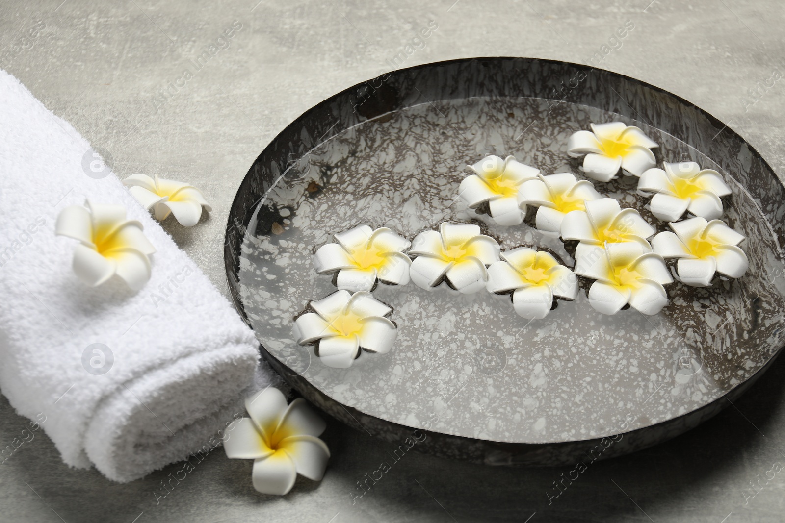 Photo of Bowl of water with flowers and towel on light grey table. Spa treatment