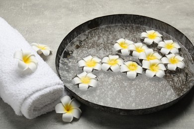 Photo of Bowl of water with flowers and towel on light grey table. Spa treatment