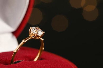 Beautiful engagement ring in red box against blurred festive lights, closeup. Space for text