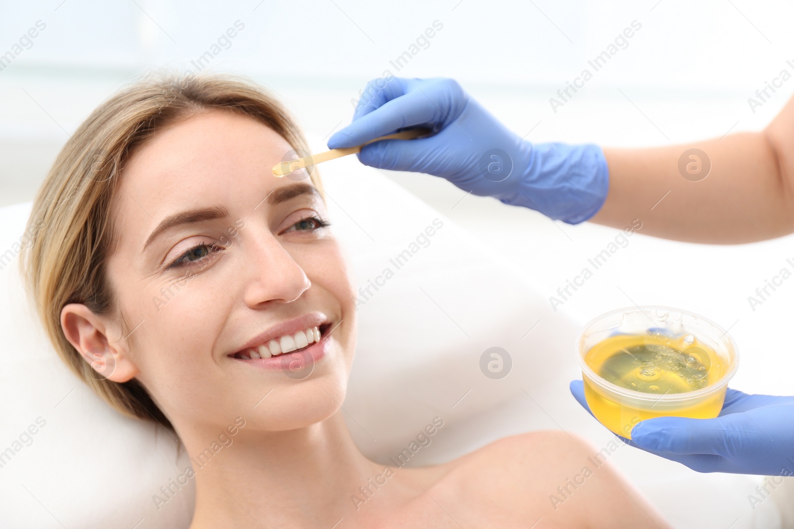 Photo of Beautiful woman getting wax epilation of face in salon