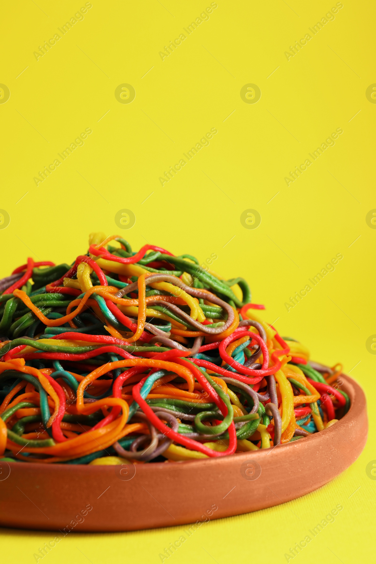 Photo of Plate of spaghetti painted with different food colorings on yellow background