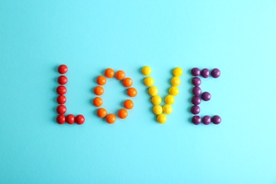 Word LOVE made of different glazed candies on light blue background, flat lay