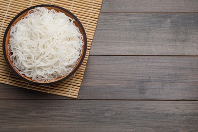 Bowl with cooked rice noodles and straw mat on wooden table, top view. Space for text