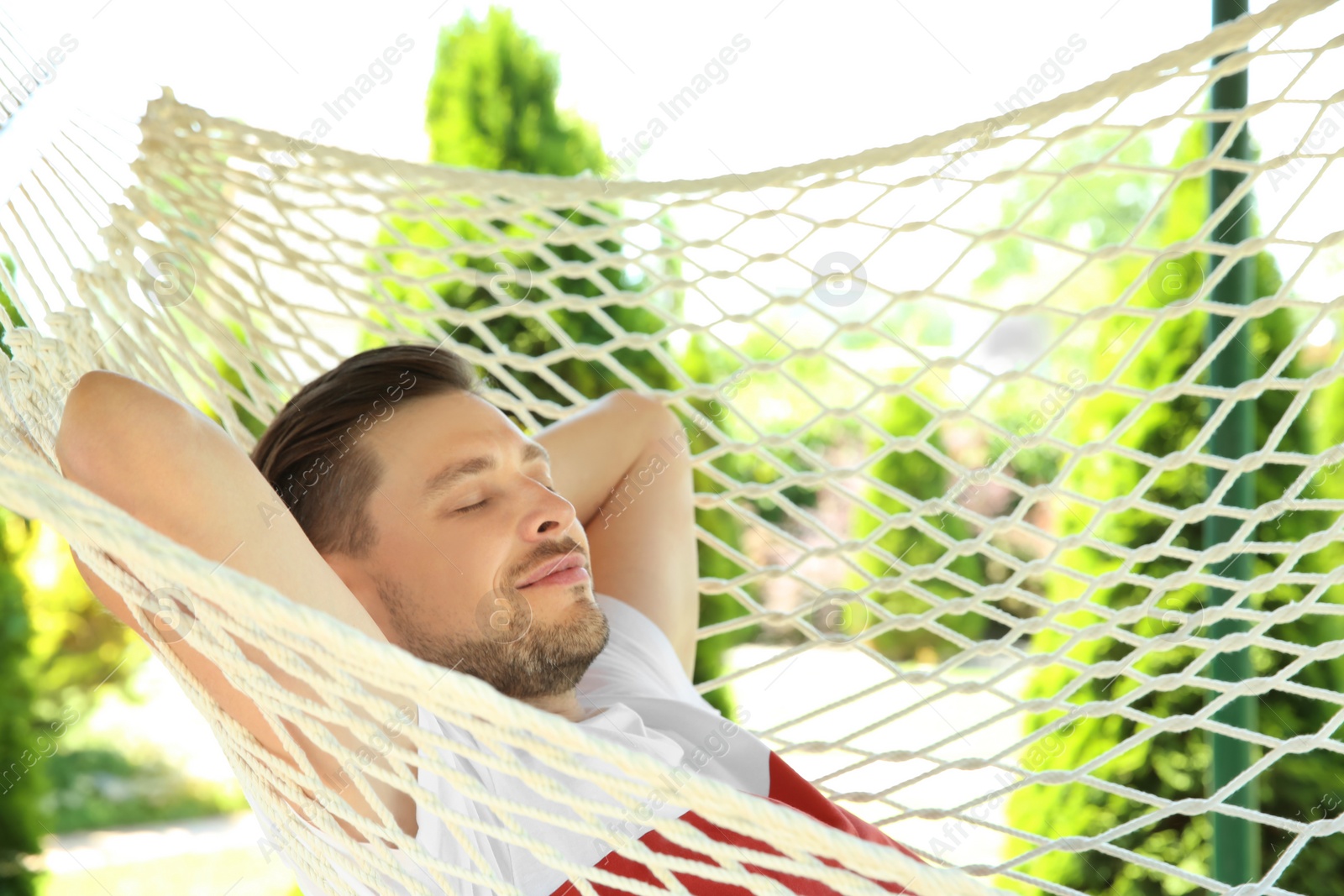 Photo of Man sleeping in hammock outdoors on warm summer day