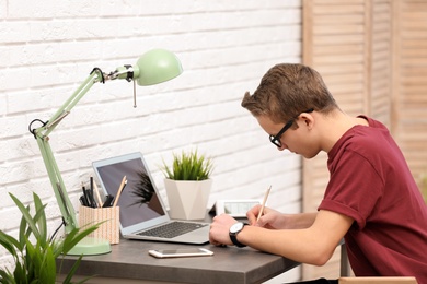 Photo of Handsome teenage boy doing homework at table in room