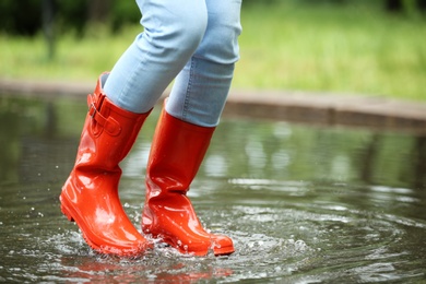 Photo of Woman with red rubber boots jumping in puddle, closeup. Rainy weather