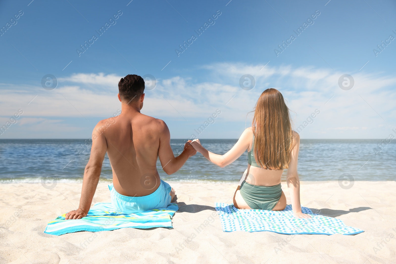 Photo of Woman in bikini and her boyfriend sunbathing on beach, back view. Lovely couple