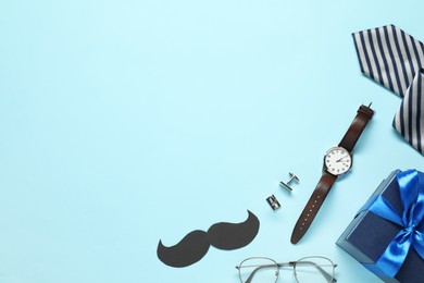 Paper mustache, gift box and men accessories on light blue background, flat lay with space for text. Father's day celebration