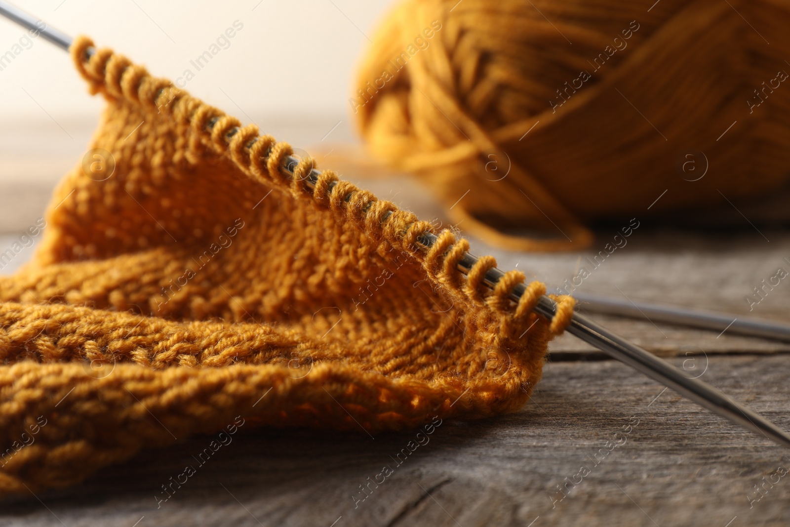 Photo of Soft orange knitting and metal needles on wooden table, closeup