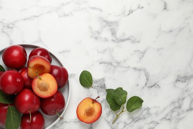 Photo of Delicious ripe cherry plums with leaves on white marble table, flat lay. Space for text