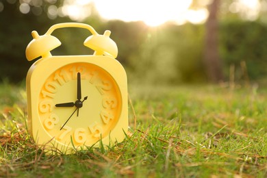 Photo of Yellow alarm clock on green grass outdoors. Space for text