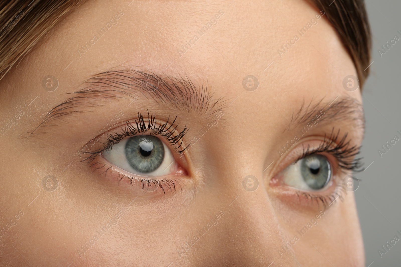 Photo of Woman with long eyelashes after mascara applying against grey background, closeup