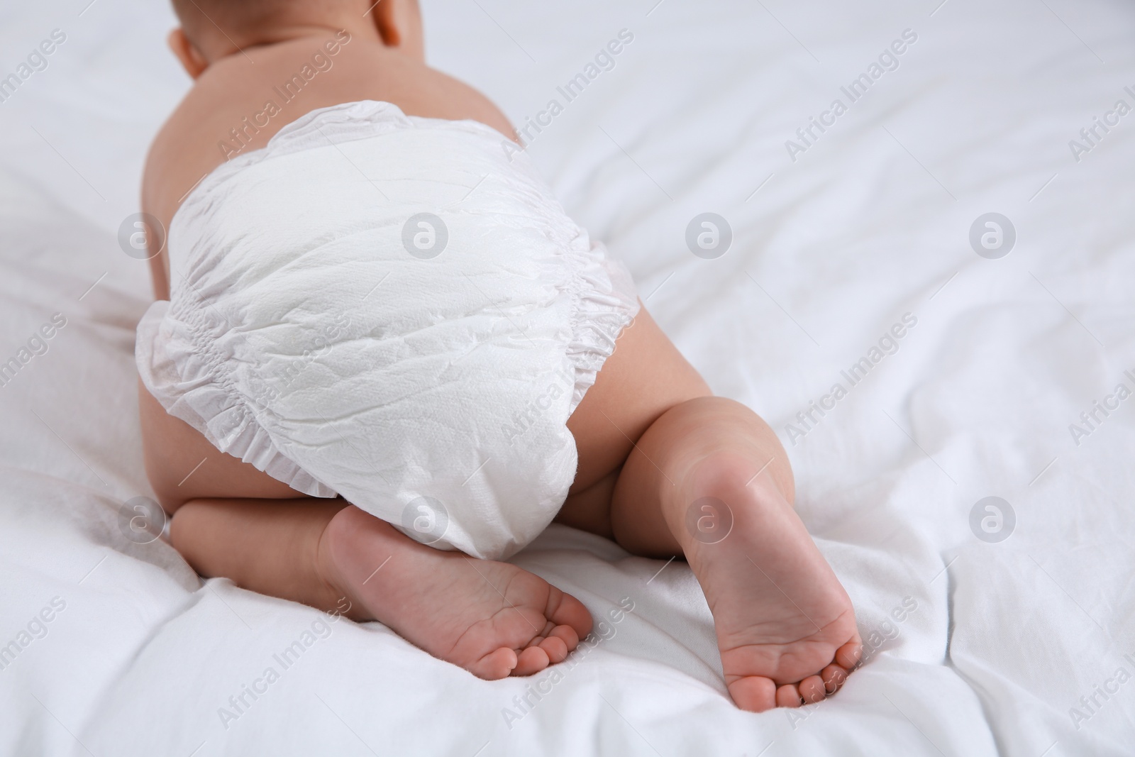 Photo of Cute baby in dry soft diaper on white bed, closeup