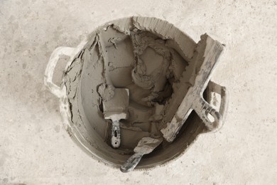 Photo of Bucket with cement and putty knifes on floor, top view