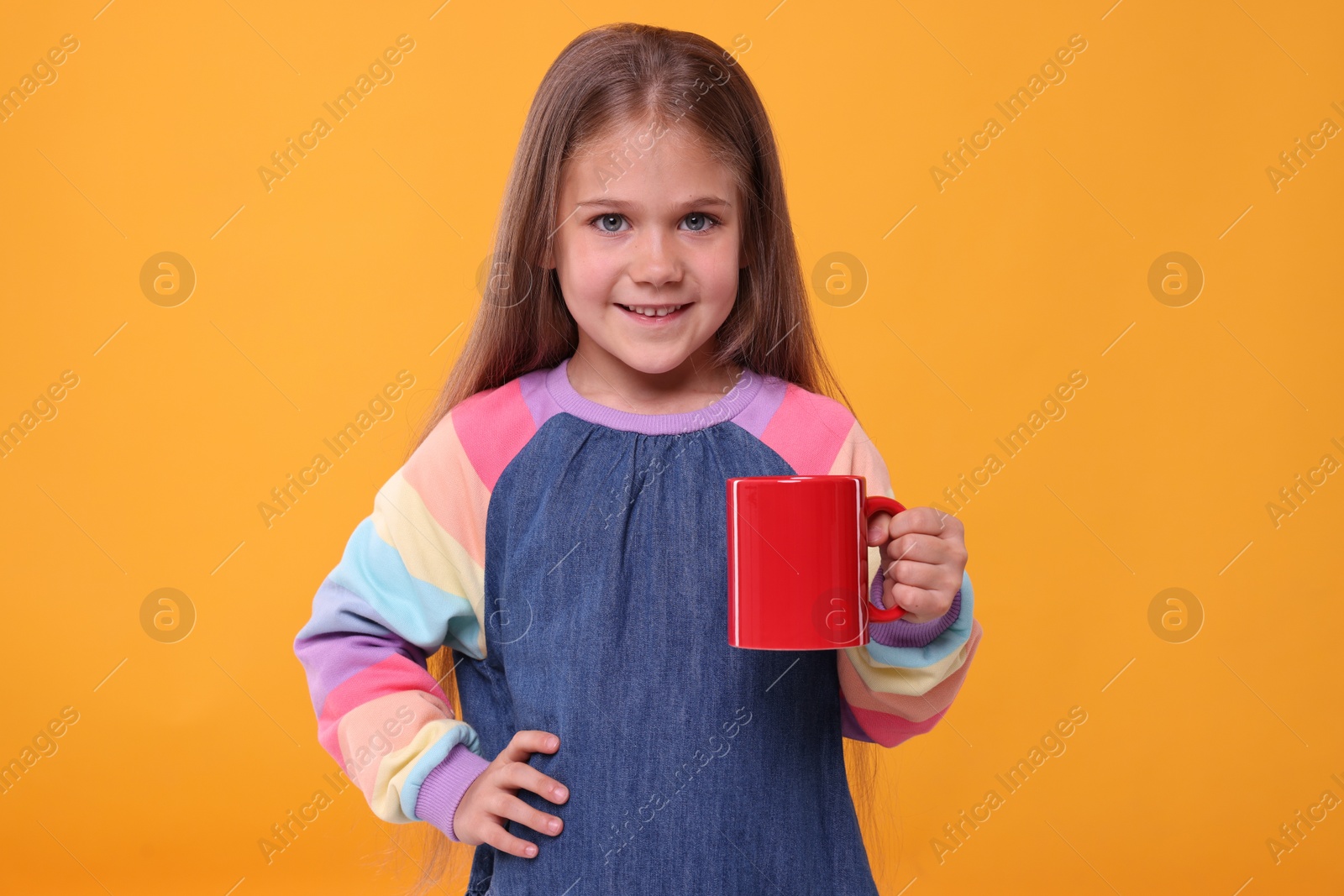 Photo of Happy girl with red ceramic mug on orange background