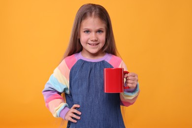 Happy girl with red ceramic mug on orange background