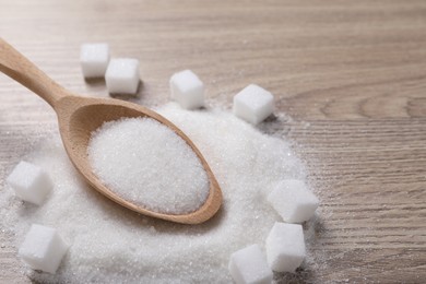 Different types of white sugar and spoon on wooden table, closeup. Space for text