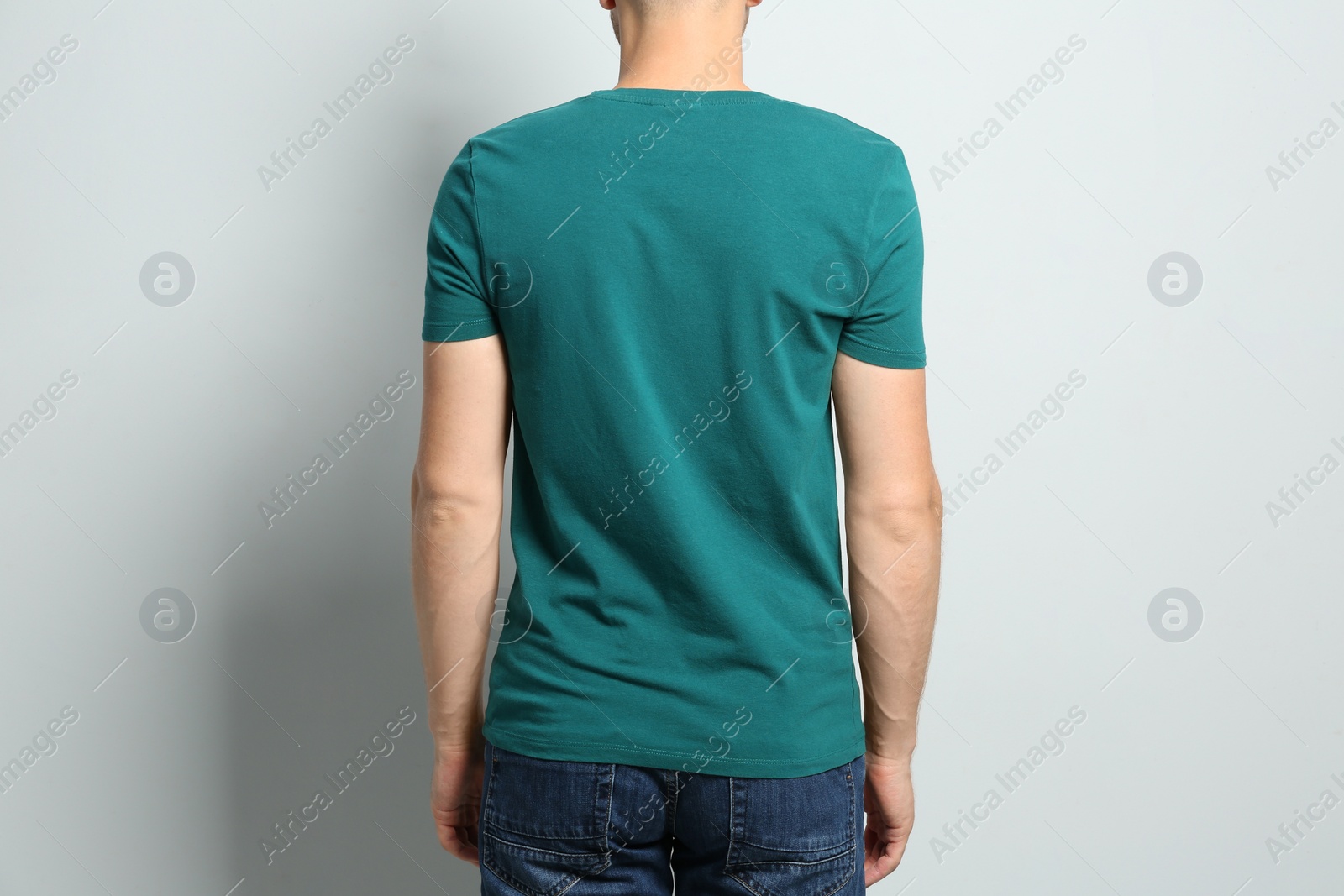 Photo of Back view of young man wearing blank t-shirt on light background, closeup. Mockup for design