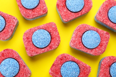 Photo of Many dishwasher detergent tablets on yellow background, flat lay