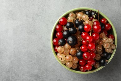 Photo of Different fresh ripe currants in bowl on light grey table, top view. Space for text