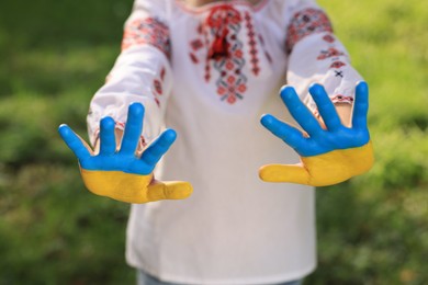 Photo of Little girl with hands painted in Ukrainian flag color outdoors, focus on palms. Love Ukraine concept