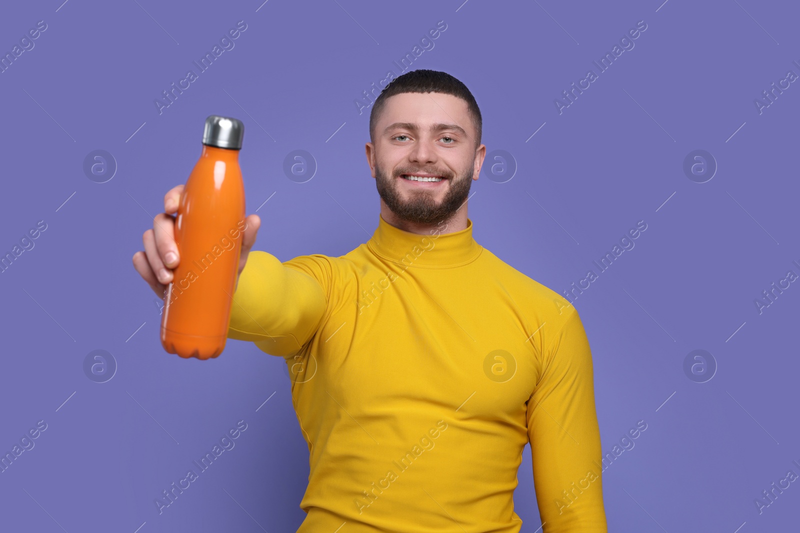 Photo of Handsome man with thermo bottle on purple background