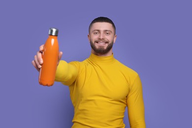 Handsome man with thermo bottle on purple background