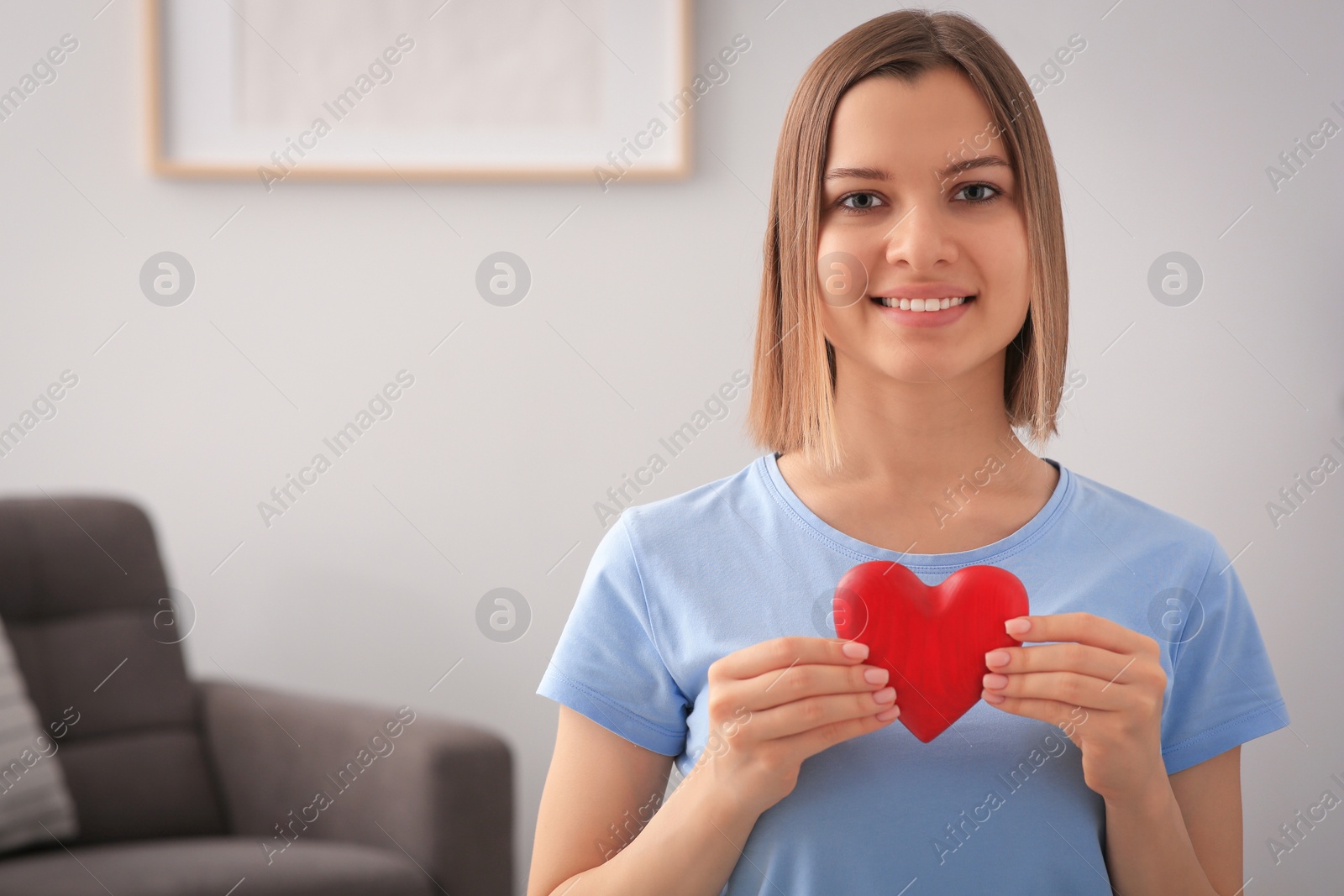 Photo of Young woman holding red heart indoors, space for text. Volunteer concept