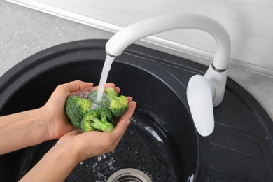 Photo of Woman washing fresh green broccoli in kitchen sink, closeup view