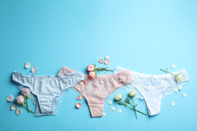 Photo of Set of elegant women's underwear and flowers on light blue background, flat lay