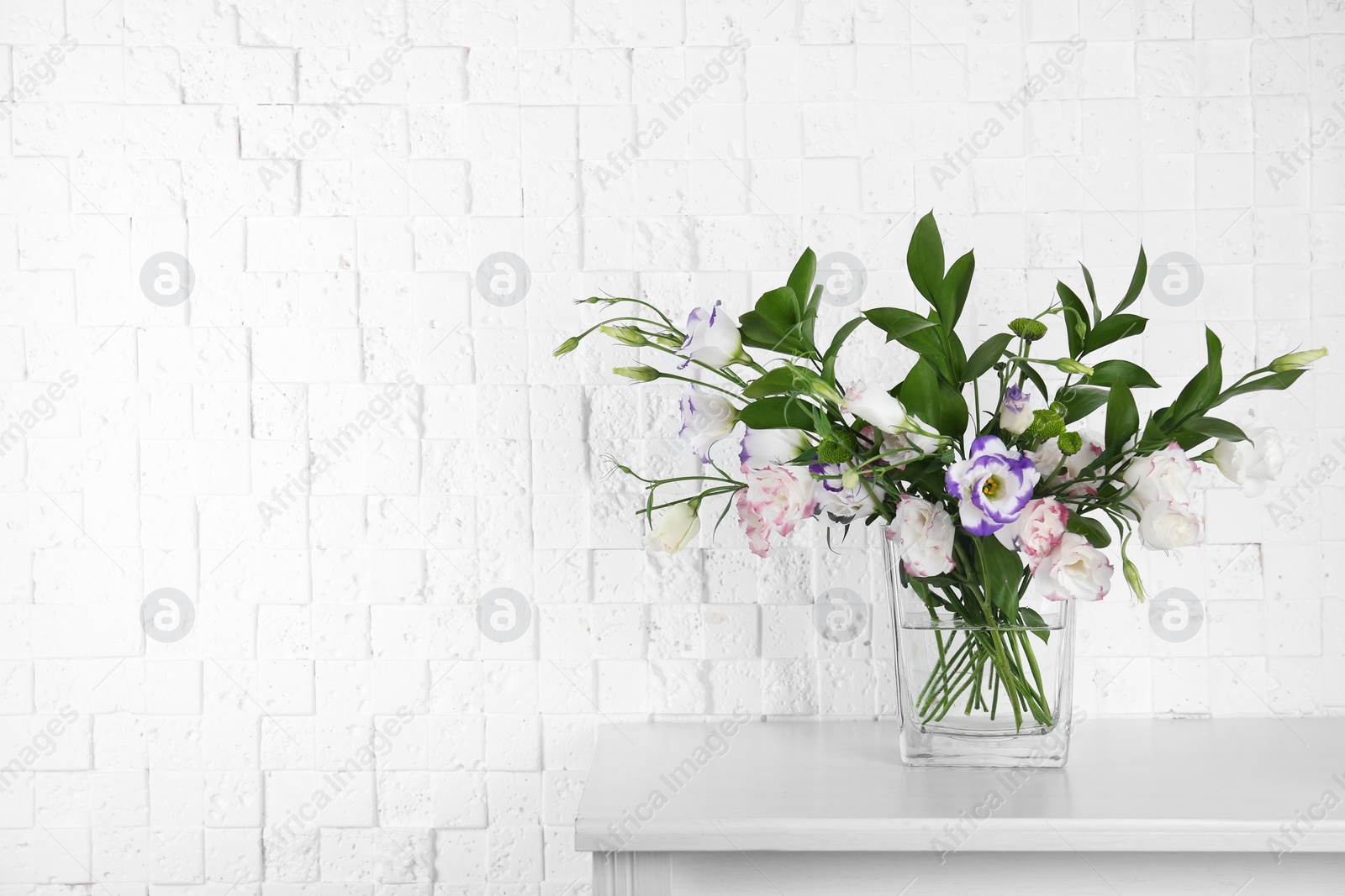 Photo of Vase with bouquet of beautiful flowers on table near brick wall. Space for text