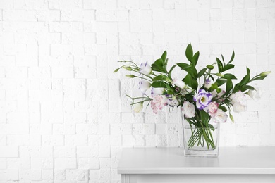 Vase with bouquet of beautiful flowers on table near brick wall. Space for text