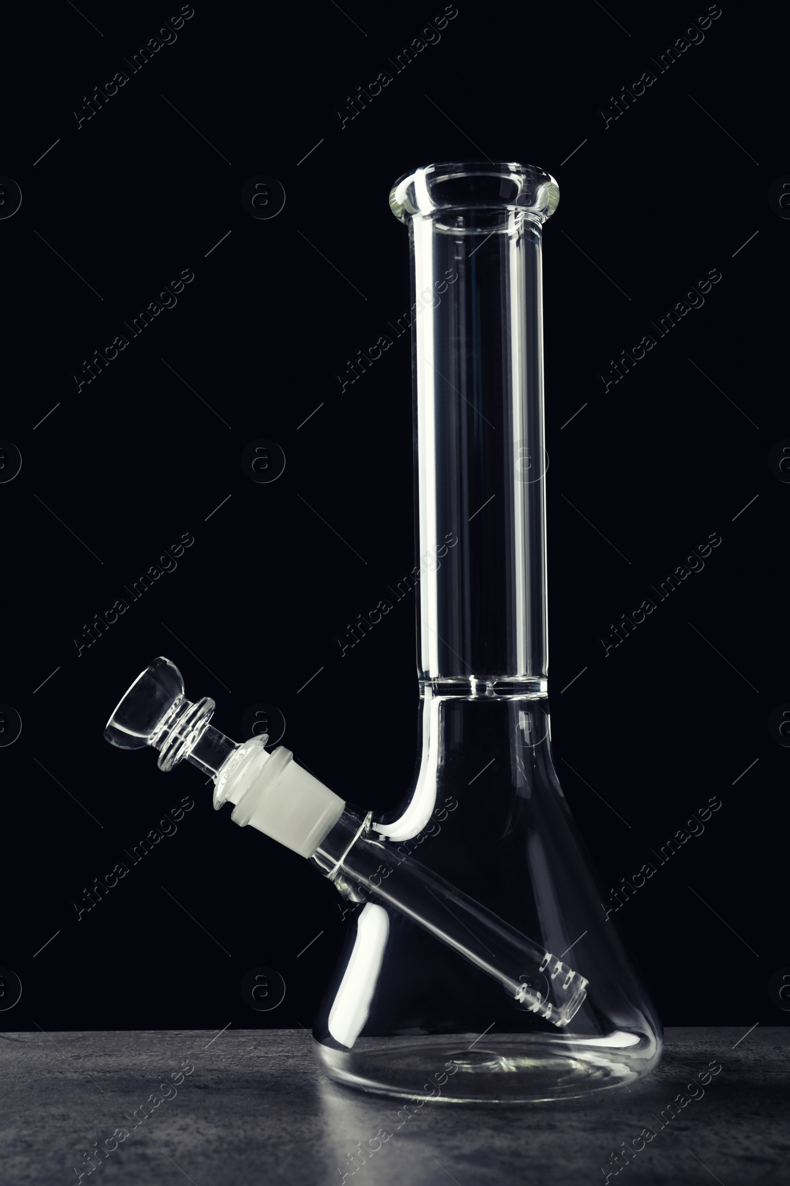 Photo of Glass bong on grey table against black background. Smoking device