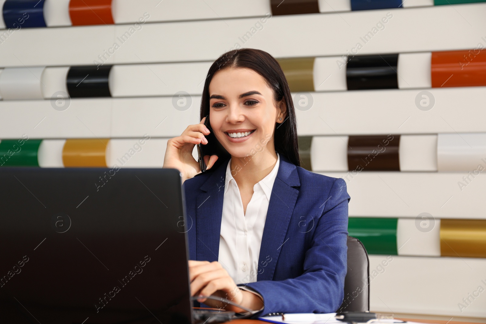 Photo of Saleswoman talking on phone at desk in car dealership