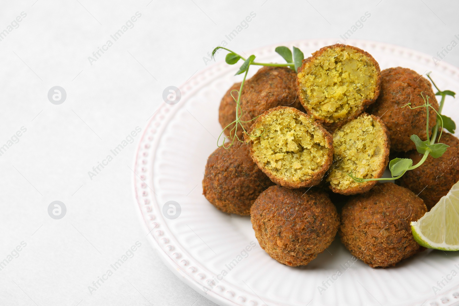 Photo of Delicious falafel balls, lime slice and microgreens on white table, closeup