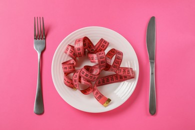 Photo of Plate, cutlery and measuring tape on pink background, flat lay. Diet concept