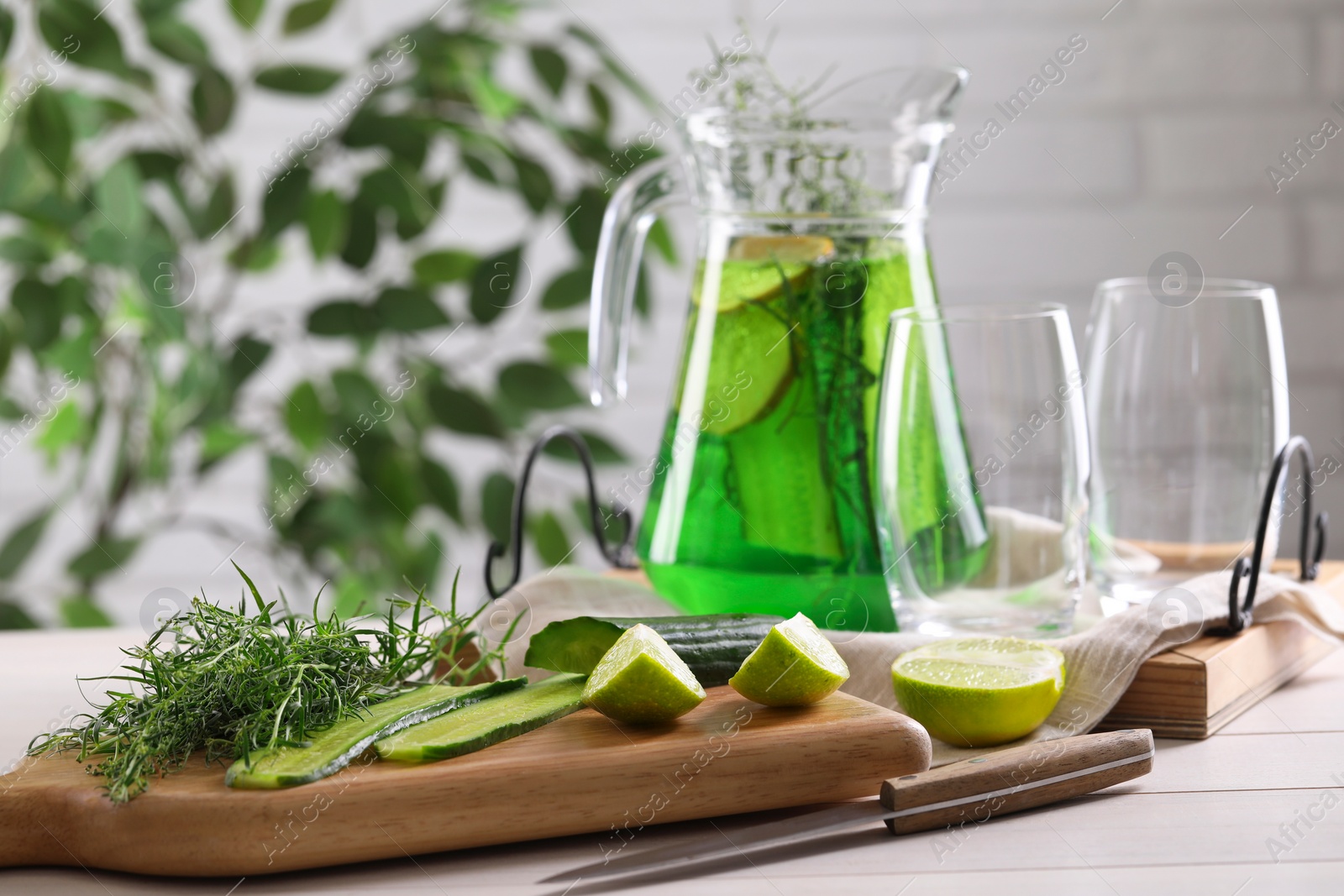 Photo of Fresh homemade refreshing tarragon drink, knife and ingredients on white wooden table, space for text