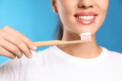 Woman holding toothbrush with paste on blue background, closeup