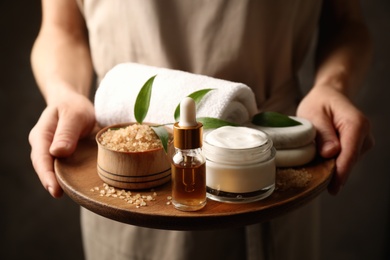 Photo of Woman holding products for spa procedures on dark background, closeup