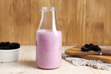 Delicious blackberry smoothie in glass bottle and fresh berries on wooden table