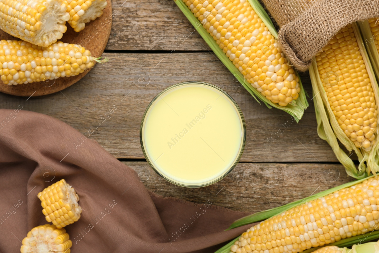 Photo of Corn juice and cobs on wooden table, flat lay