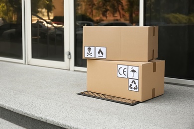 Cardboard boxes with different packaging symbols on door mat near entrance. Parcel delivery